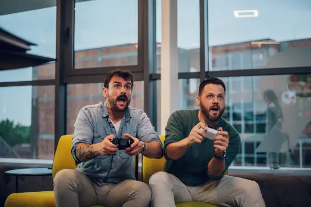 Team members of a business company spending their free time together while playing video games during their work break. Testing new game. Two male colleagues playing video games together.