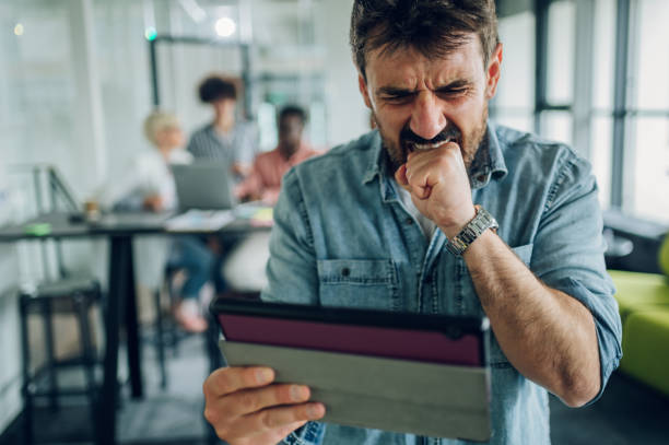 istock Angry business man using tablet in the office with his team working in the back 1397623046
