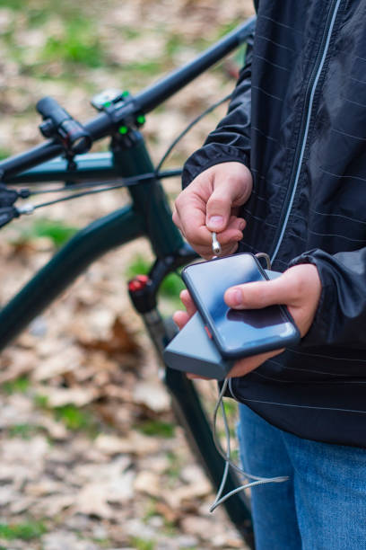 A tourist charges a smartphone with a power bank on the background of a bicycle in nature. A tourist charges a smartphone with a power bank on the background of a bicycle in nature bicycle docking station stock pictures, royalty-free photos & images