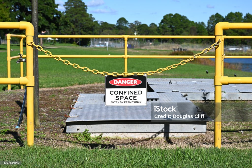 Danger confined space sign Danger confined space sign on a fence around a man hole Confined Space Stock Photo