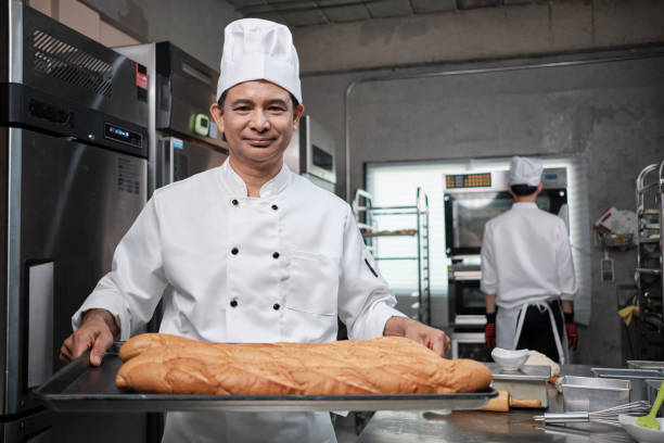 el chef senior mostró pan fresco con una sonrisa en la cocina de acero inoxidable. - commercial kitchen bakery front view baking fotografías e imágenes de stock