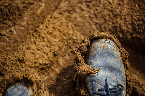 Old dirty boots on the ground, full of clay and mud at the boots.