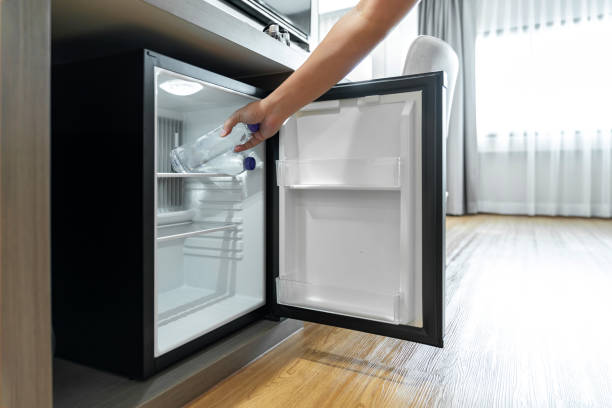 man hand opened mini small refrigerator and reached drinking plastic water bottle under the wood counter in the hotel resort bedroom. - plastic fles klein stockfoto's en -beelden