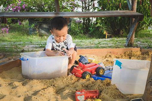 Cute Asian baby boy digging sand on the playground. Happy little child playing while on vacation in summer holiday. Kid playful in nature at the park. Copy space