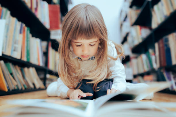 bambina intelligente che controlla un libro in biblioteca - searching child curiosity discovery foto e immagini stock