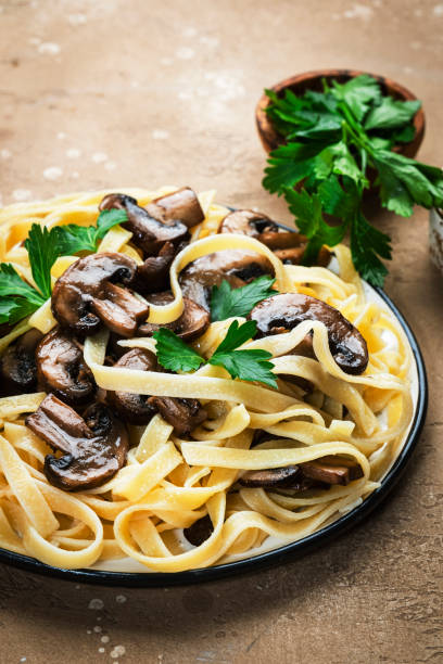istock Cooked pasta with mushrooms with parsley on plate on beige stone kitchen table background, top view. Vegan cooking and eating, italian cuisine recipe 1397645180