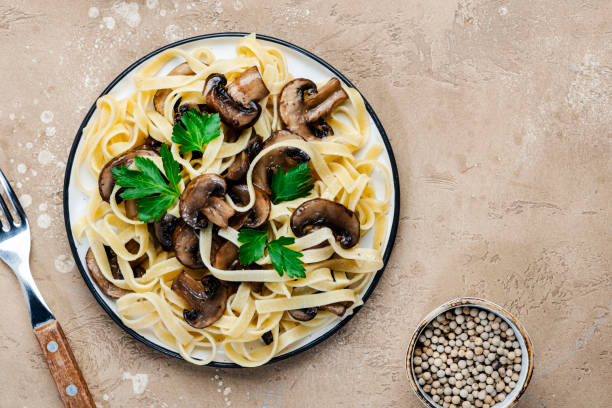 istock Cooked pasta with mushrooms with parsley on plate on beige stone kitchen table background, top view. Vegan cooking and eating, italian cuisine recipe 1397645183