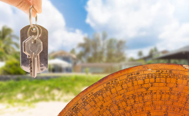 ключ от дома в руке девушки с древним компасом фэн-шуй на размытом фоне дома - fengshui стоковые фото и изображения
