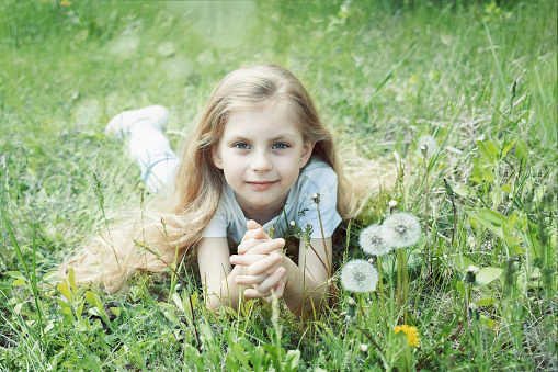 Image of pretty little girl lying down on dandelions field, happy cheerful girl resting on dandelions meadow, relaxation outdoor in springtime, vacation
