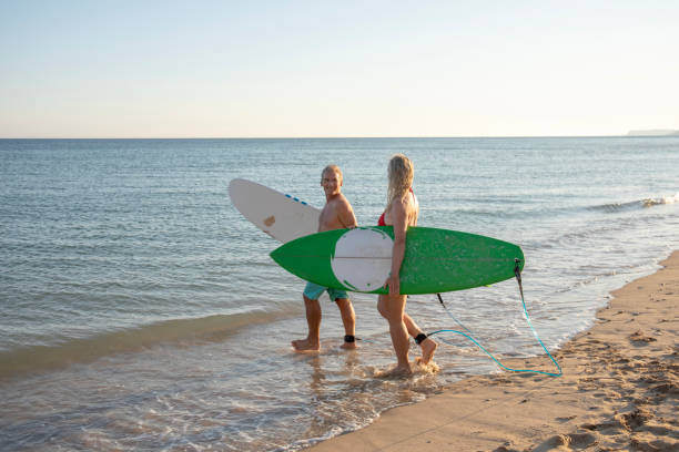 istock Couple carry surfboards into tranquil sea 1397654260