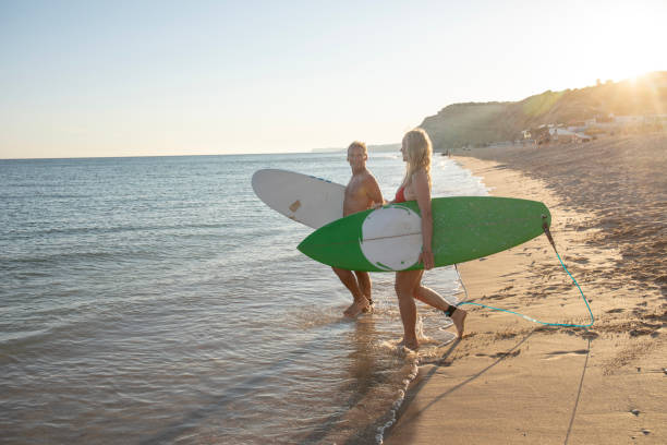 istock Couple carry surfboards into tranquil sea 1397654278