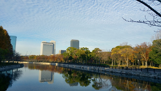 The canal around the Osaka Castle Park. Facing the city area and business buildings. Cloudy blue sky and canal reflection of buildings. Beautiful evening golden sunset light. Osaka, Japan.