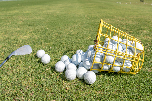 A golf club and a basket of golf balls on the lawn of a golf course