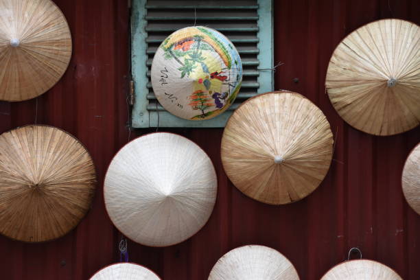 Medium shot of a red steel wall hung with a collection of Vietnamese conical ‘non la’ hats