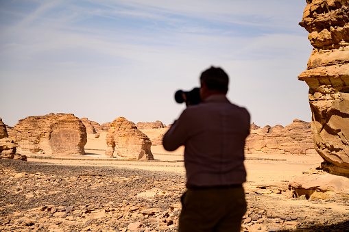 Rear view of man with camera and focus on red sandstone outcrops, including Elephant Rock, shaped by wind and water erosion over millions of years.