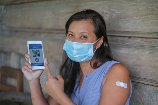 Close-up shot of Vietnamese woman with surgical mask showing her digital certificate of COVID-19 vaccination from smartphone.