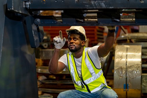 African American mechanic worker is checking the gear for hydraulic machine inside metal steel manufacturing factory for maintenance and inspection