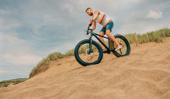 Young man riding a fat bike through the beach dunes