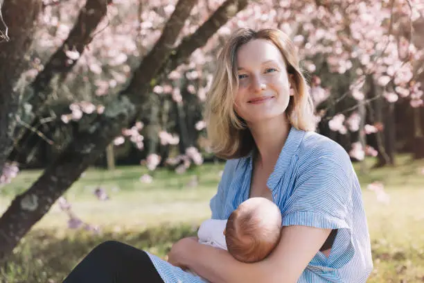 Beautiful mother breastfeeding baby. Young woman breast feeding her newborn baby. Concept of lactation infant, postpartum period, natural motherhood. Mother and baby on nature outdoors.