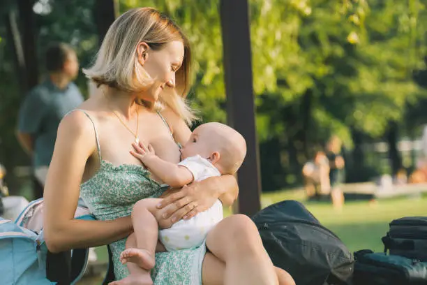 Beautiful mother breastfeeding baby. Young woman breast feeding her newborn baby. Concept of lactation infant, postpartum period, natural motherhood. Mother and baby on nature outdoors.