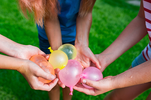 Close up cropped girls holding water balloons in hands. Joint games with water for kids. Summer fun outdoor activities for children concept.