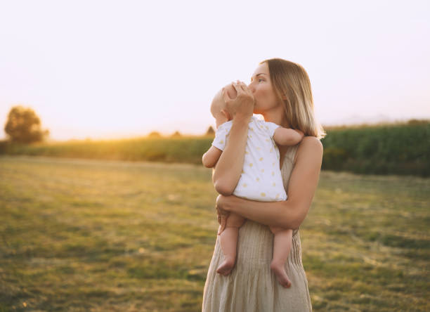 loving mother and baby at sunset. beautiful woman and small child in nature background. concept of natural motherhood. happy healthy family at summer outdoors. positive human emotions and feelings. - healthy lifestyle nature sports shoe childhood imagens e fotografias de stock