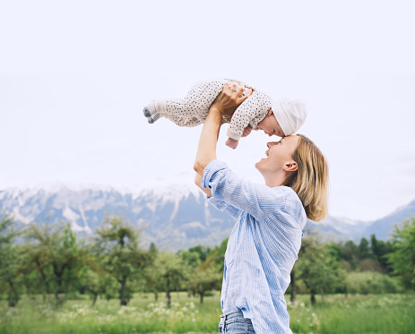 Mother and baby walking on nature outdoors. Family in green nature background. Loving woman with child in countryside. Concept of green parenting, natural motherhood, postpartum period.