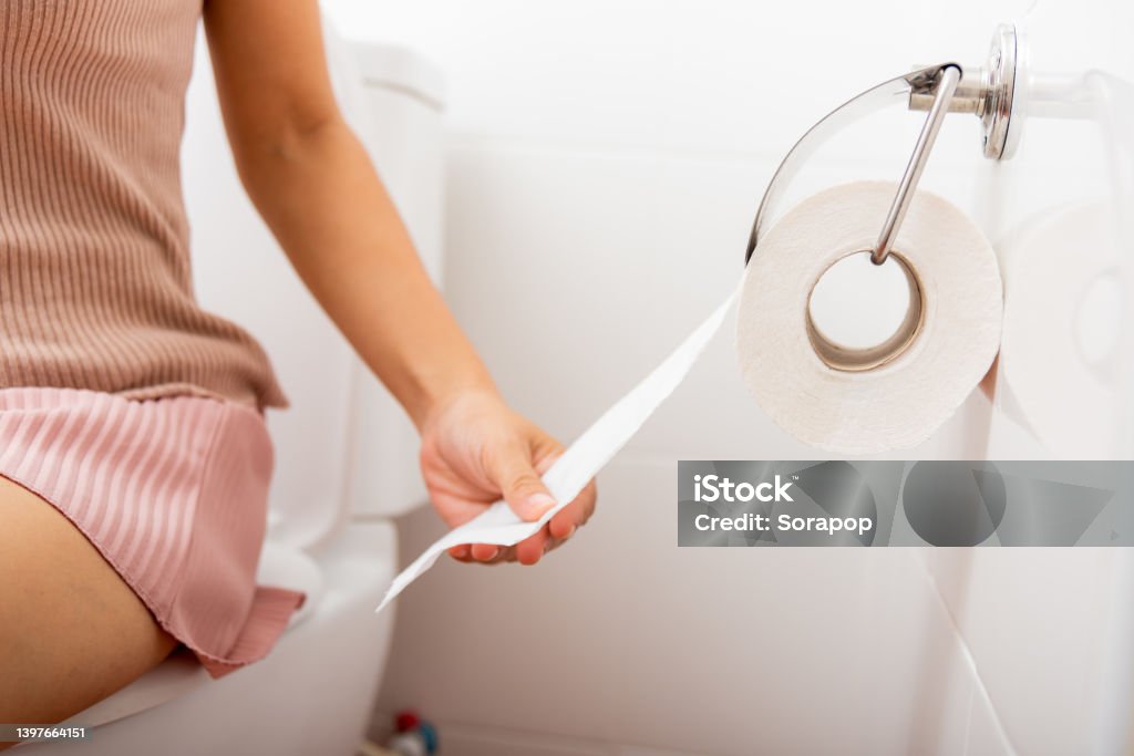 Closeup hand pulling toilet paper roll in holder for wipe	Closeup hand pulling toilet paper roll in holder for wipe, woman sitting on toilet she taking and tearing white tissue on wall to towel clean in bathroom, Healthcare concept Closeup hand pulling toilet paper roll in holder for wipe, woman sitting on toilet she taking and tearing white tissue on wall to towel clean in bathroom, Healthcare concept Toilet Stock Photo