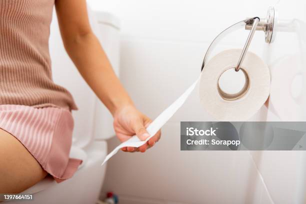 Closeup Hand Pulling Toilet Paper Roll In Holder For Wipe Closeup Hand Pulling Toilet Paper Roll In Holder For Wipe Woman Sitting On Toilet She Taking And Tearing White Tissue On Wall To Towel Clean In Bathroom Healthcare Concept Stock Photo - Download Image Now
