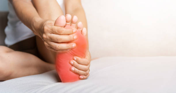 Asian woman sitting on sofa feeling pain in her foot at home stock photo