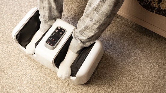 Foot massager. A man relaxes during a foot massage at home. Close-up of an electric massager device.