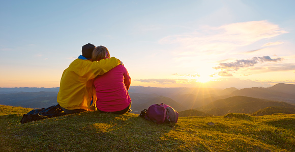 Rear view of mature couple sitting on top of mountain while looking at view.