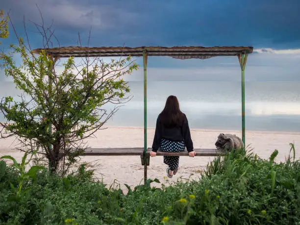 Photo of Rear view of a woman sitting on a bench in front of the sea.