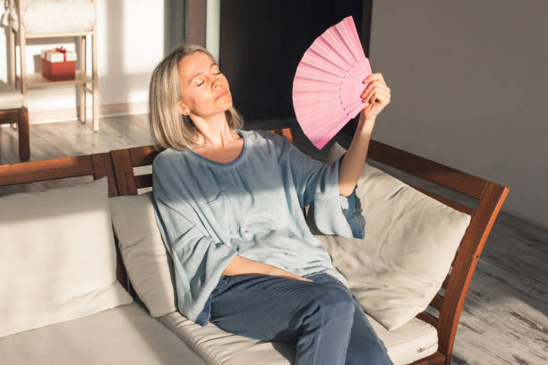 istock Exhausted middle aged woman using paper waver, suffering from hot summer 1397670652