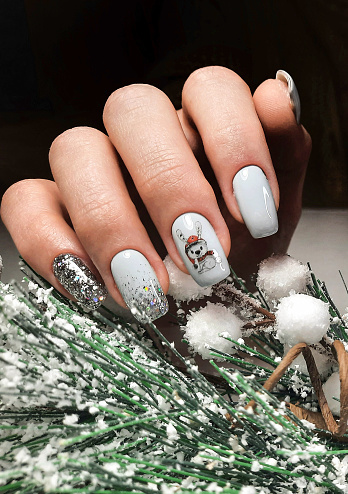 Una manicura pulcra con un delicado diseño en color pastel con una rama de árbol de Navidad cubierta de nieve. Uñas largas cuadradas con esmalte en gel y diseño de liebre y brillos photo