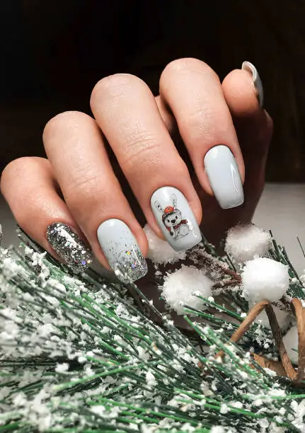 A neat manicure with a delicate design in pastel color with a christmas tree branch covered with snow. Long square nails with gel polish and hare design and glitters