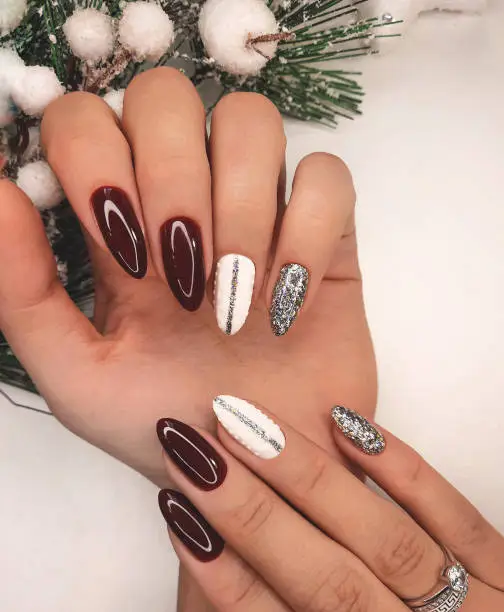 A neat manicure  with a christmas tree branch covered with snow. Long round nails with red gel polish and  white design and silver glitters