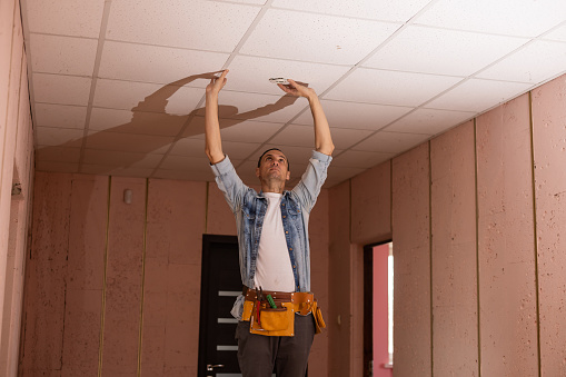 Man in builder uniform hand up installing suspended ceiling.