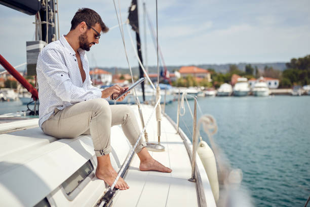 istock A young man is sitting on a yacht and using a tablet while riding through the dock on the seaside. Summer, sea, vacation 1397677299