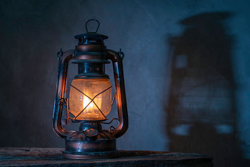 antique kerosene lamp with lights on the wooden floor in the gray old plaster background. soft focus.