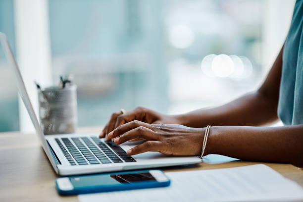 close-up de uma empresária negra digitando em um teclado portátil em um escritório sozinho - typing - fotografias e filmes do acervo