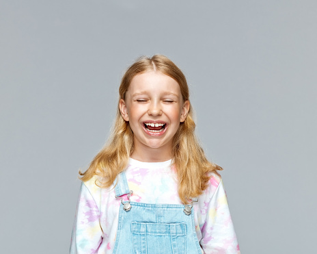 Girl in casuals laughing with eyes closed against gray background