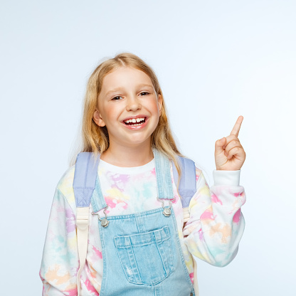 Portrait of happy schoolgirl in casuals pointing while standing against white background