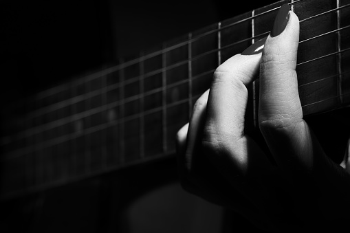 female hand with guitar strings plays closeup monochrome