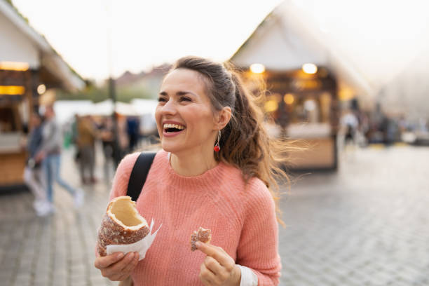 smiling 40 years old woman at fair in city eating trdelnik smiling modern 40 years old woman at the fair in the city eating trdelnik. trdelník stock pictures, royalty-free photos & images