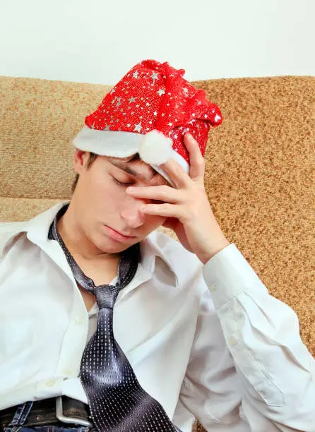 Sad and Tired Young Man in Santa Hat on the Sofa at the Home