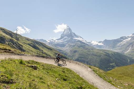 Man on mountain bike riding on flow trail, Matterhorn mountain peak in distance, Switzerland.