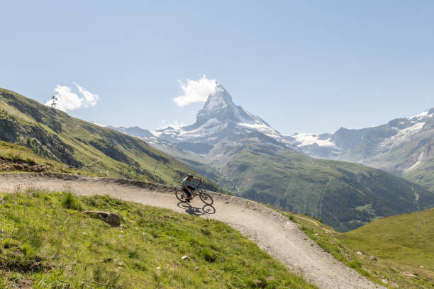 Man on mountain bike riding on flow trail, Matterhorn mountain peak in distance, Switzerland. biker on dirt trail, Switzerland stock photo