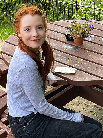 Stock photo showing a young red-headed woman sitting outdoors, in the garden of a pub.