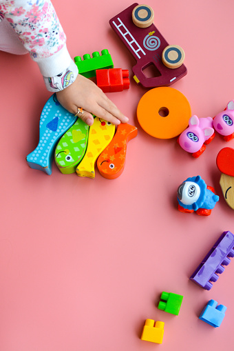 Child is playing with colorful wooden and plastic toys, on pink background